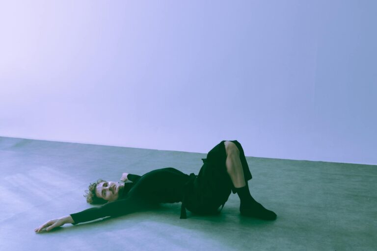 A person in a creative pose on the studio floor, highlighting minimalist aesthetics and expressive art.