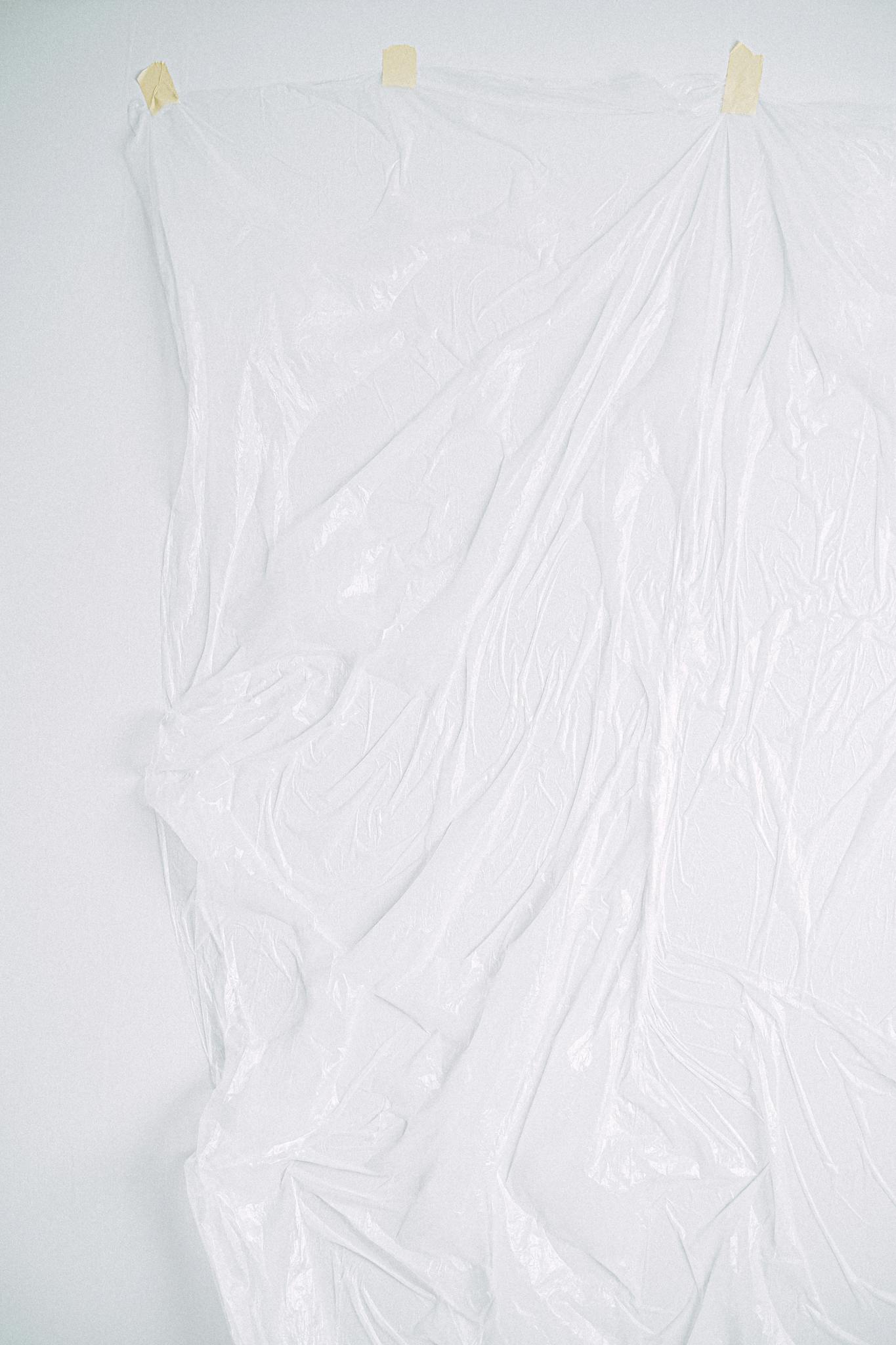 A texture-rich white plastic sheet taped on a wall, ideal as a minimalist background with ample copy space.